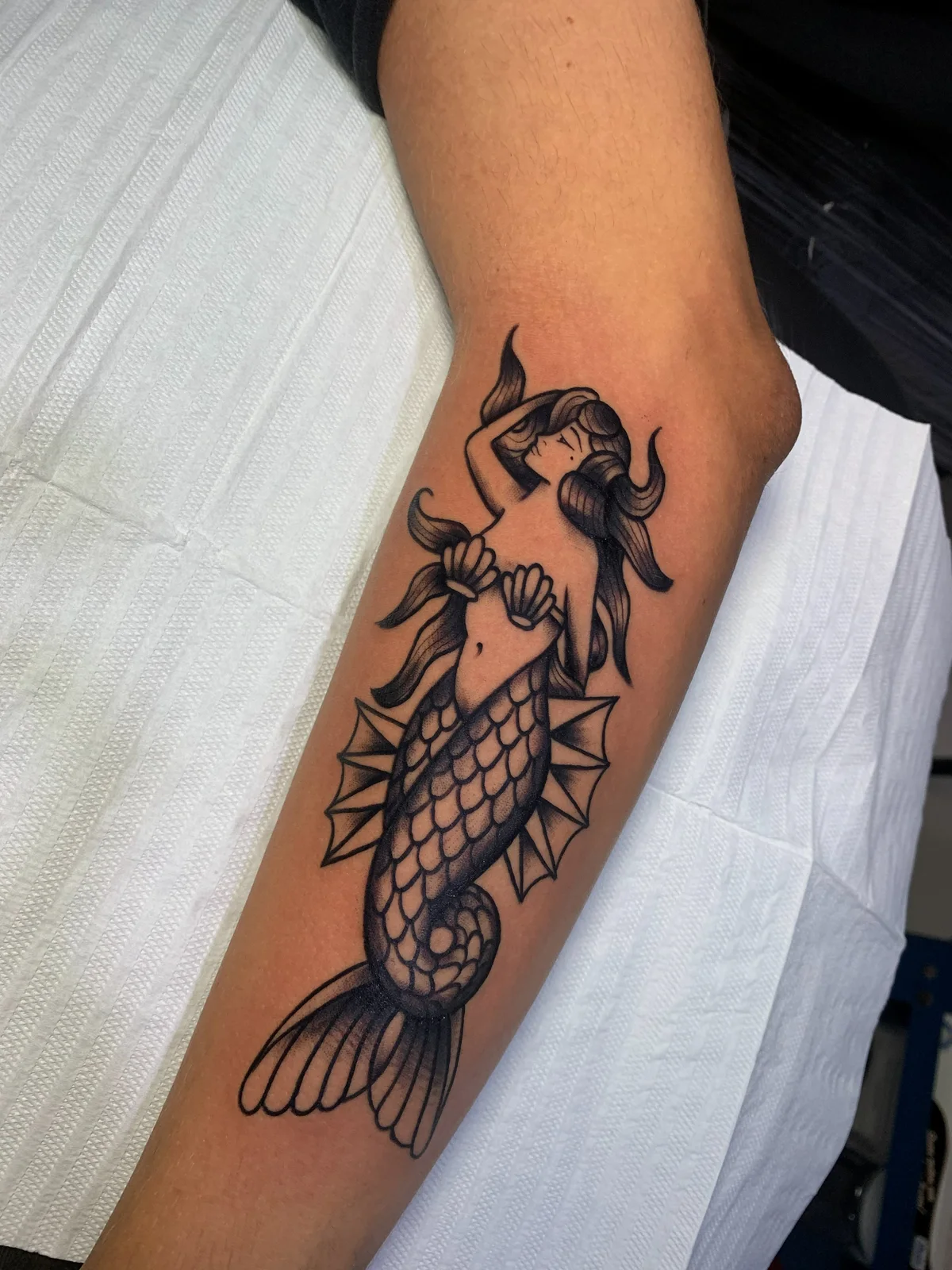 Black-outline mermaid tattoo on the forearm