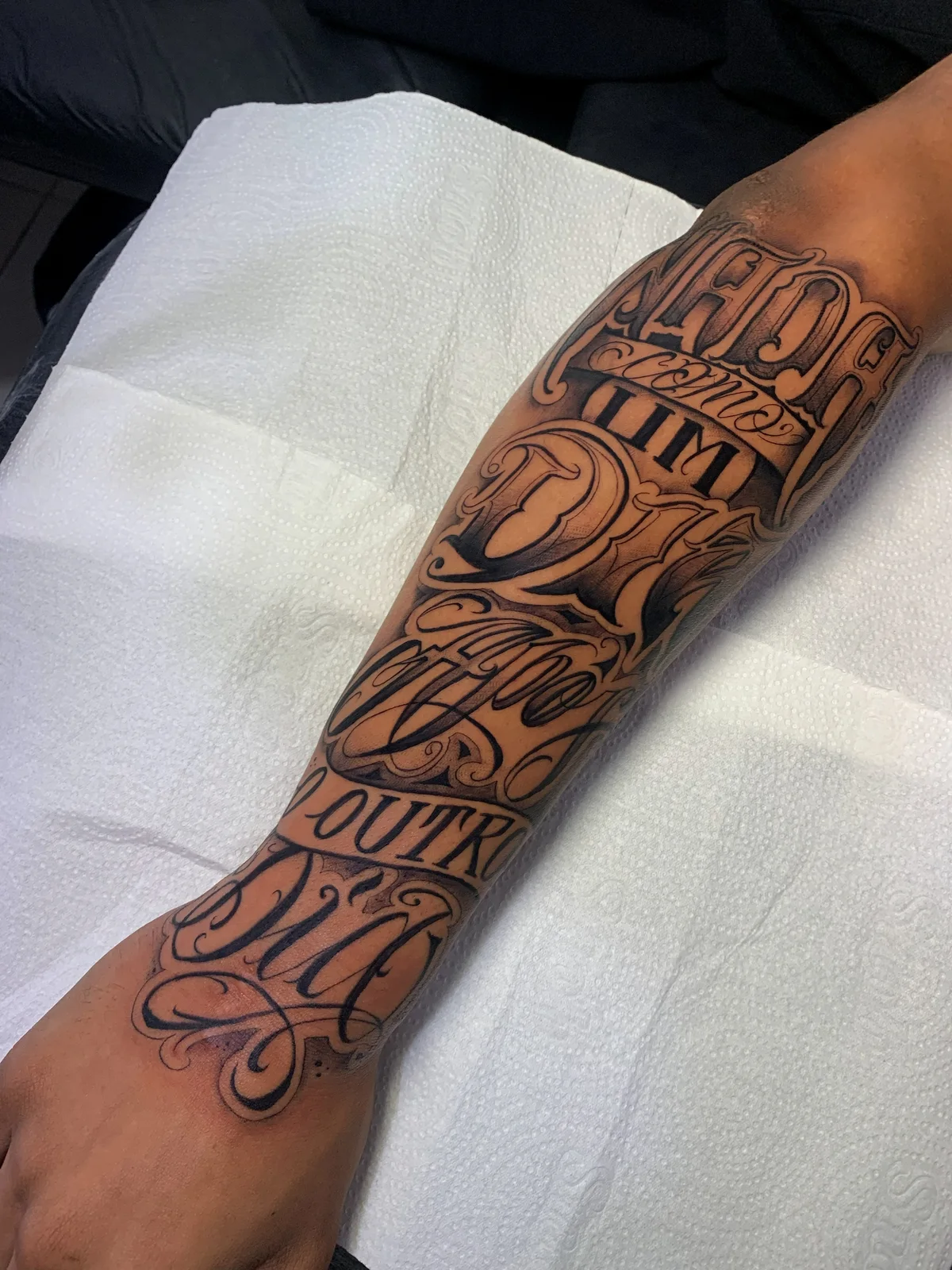 Black and grey chicano lettering on the forearm